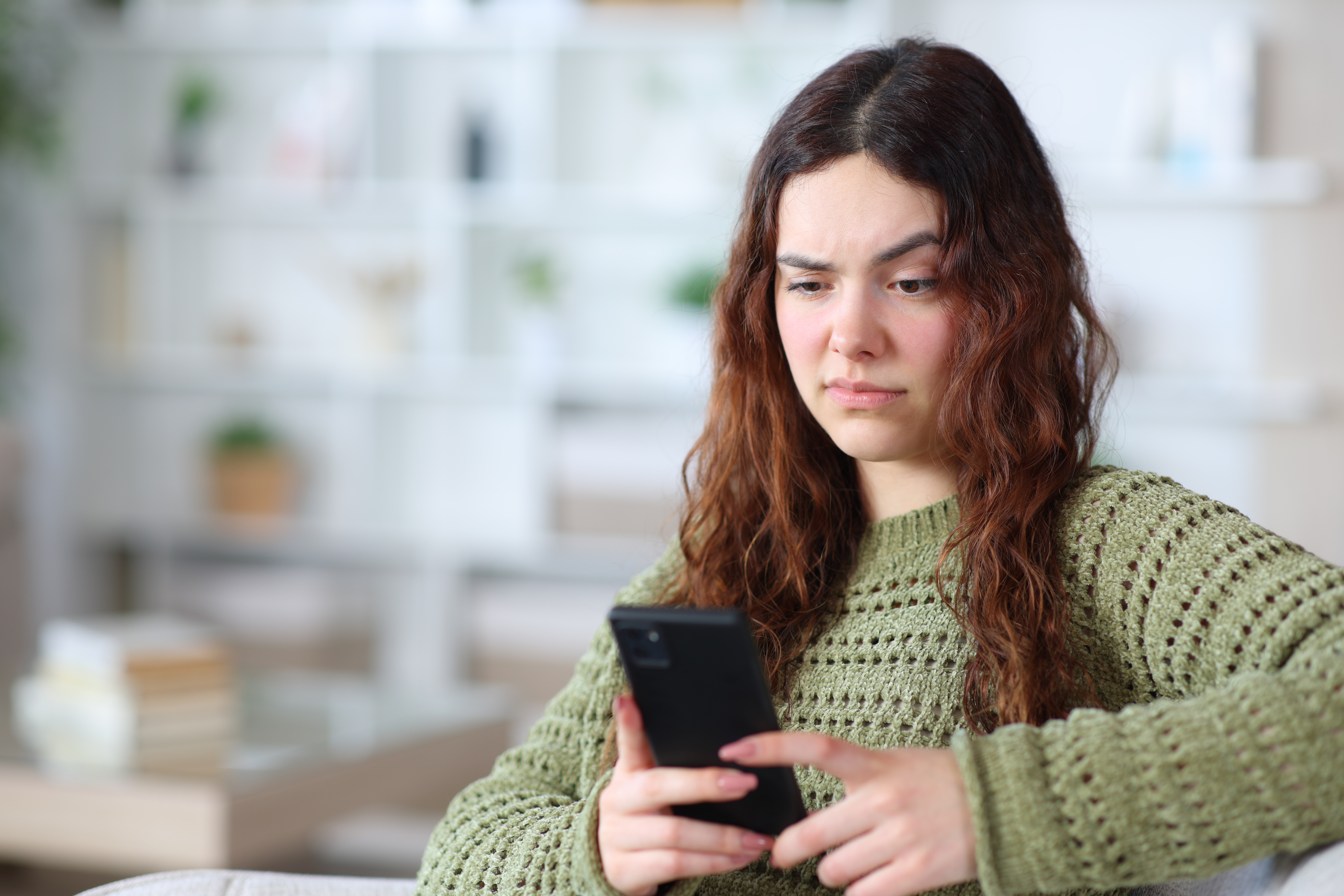 Young woman looking suspiciously at her cell phone